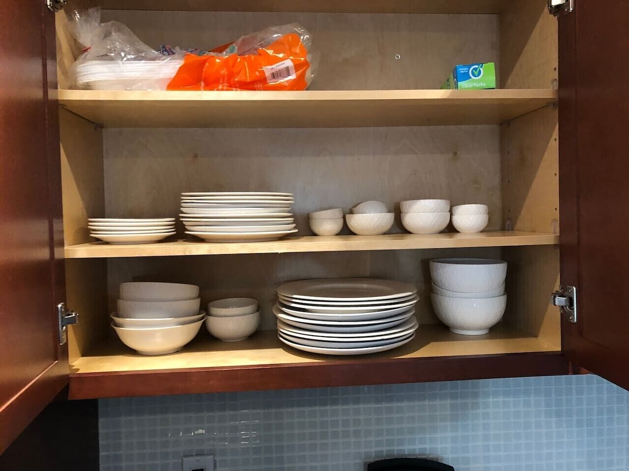 Un armadietto da cucina con ripiani che contengono piatti, ciotole e un sacchetto di plastica.