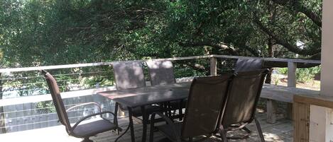 An outdoor patio with a table and chairs, surrounded by a wooden deck and a metal railing.