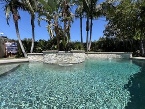 Una piscina cristalina rodeada de muros de piedra y palmeras.