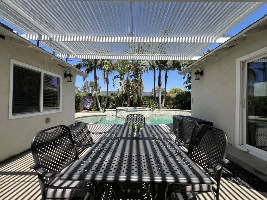 Une terrasse extérieure avec une piscine, un espace salon couvert et une vue sur les palmiers.