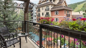 Un balcón con vistas a una piscina, rodeado de flores de colores y un edificio con varios balcones.
