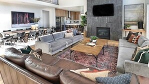 Ein geräumiges Wohnzimmer mit hoher Decke, einem großen Flachbildfernseher an einer Steinwand und einer gemütlichen Sitzecke mit Ledersofas und einem Couchtisch.