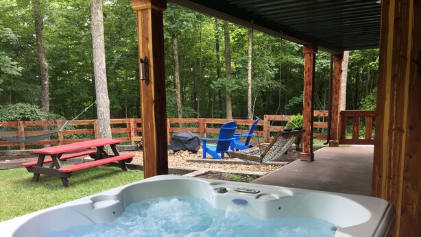 Een hottub met een houten terras, picknicktafel en blauwe stoelen in een bebost gebied.