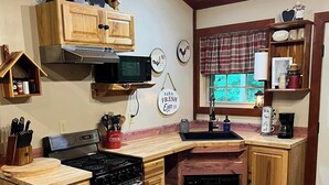Een keuken met houten kastjes, een kookplaat, een magnetron en een spoelbak. Er staan decoratieve objecten aan de muur en er ligt een vloerkleed.