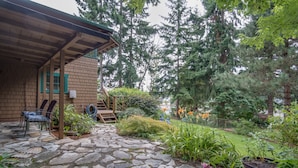 A stone-paved patio with a wooden pergola, outdoor seating, and lush greenery. - PEACEFUL WATERFRONT RETREAT 30-MINUTE FERRY RIDE FROM SEATTLE! (Bremerton)