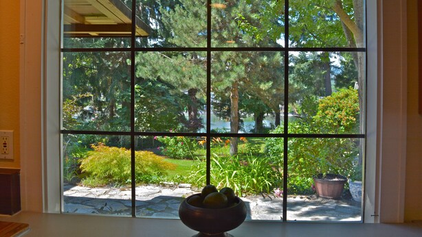 A window with a grid pattern, through which a garden with various plants and a pond is visible. - PEACEFUL WATERFRONT RETREAT 30-MINUTE FERRY RIDE FROM SEATTLE! (Bremerton)