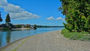 A riverside view with houses along the water, a gravel path, and dense greenery. - PEACEFUL WATERFRONT RETREAT 30-MINUTE FERRY RIDE FROM SEATTLE! (Bremerton)