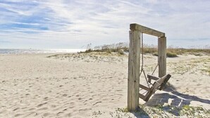 A wooden swing set on a sandy beach with a clear sky.