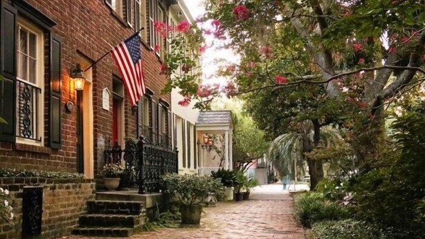 A brick building with an American flag, a brick pathway, and lush greenery.