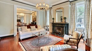 A spacious living room with a fireplace, a chandelier, and a large mirror.