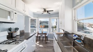 A modern kitchen with white cabinets, a gas stove, a sink, and a dining area with a table and chairs. - Pacific Bungalow | Ocean View with Tiny House! (Oceanside)