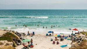 A beach with people swimming and sunbathing, umbrellas, and beach chairs. - Pacific Bungalow | Ocean View with Tiny House! (Oceanside)
