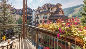 A balcony with a table and chairs, a flower arrangement, and a view of traditional buildings and a mountainous landscape.