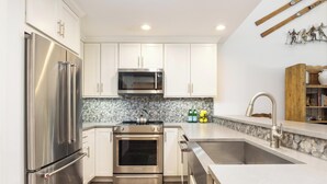 A modern kitchen with stainless steel appliances, white cabinetry, a stone backsplash, and a built-in oven.