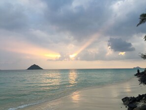 A beach with calm waters, a distant island, and a cloudy sky.