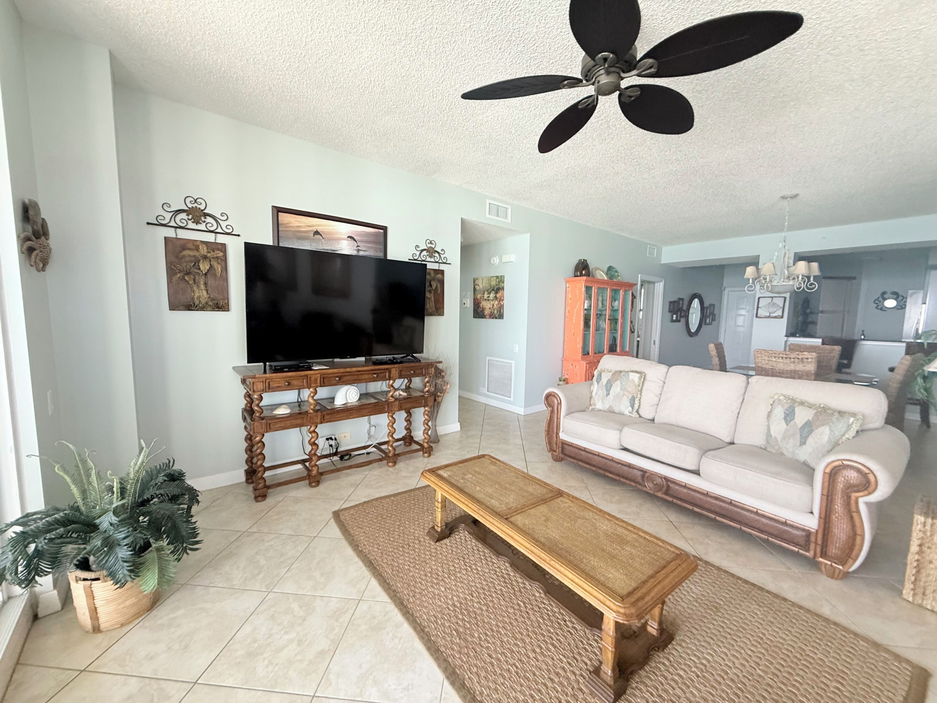 A living room with a television on a wooden stand, a sofa, a coffee table, and a ceiling fan.