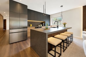 A modern kitchen with dark cabinetry, a central island with bar stools, and a large window providing a view.
