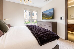 Une chambre d’hôtel moderne dotée d’un grand lit, d’un téléviseur à écran plat, d’une fenêtre donnant sur des immeubles et d’une armoire en bois.
