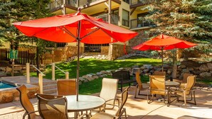 An outdoor patio area with round tables and chairs, red umbrellas, and a pool. - Montaneros 302 - 3 Bedroom Platinum (Vail)