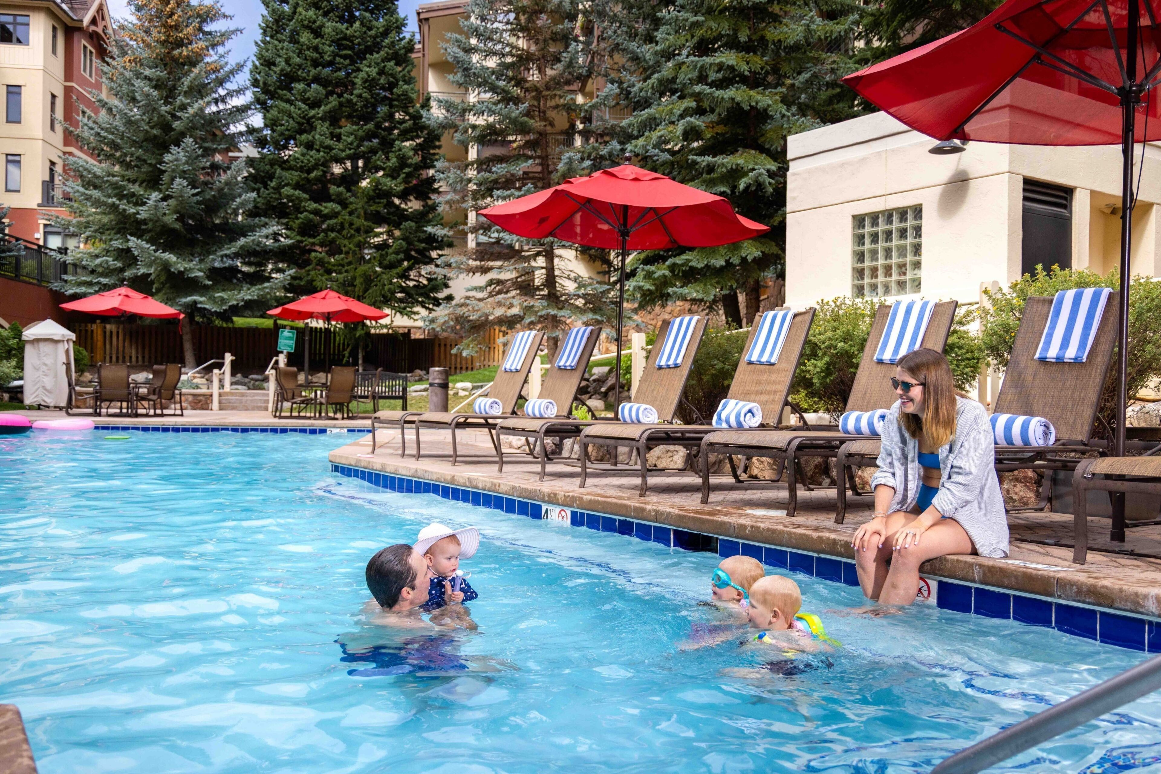 A swimming pool area with lounge chairs and red umbrellas.