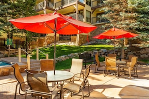 Un espace extérieur aménagé en terrasse, avec des tables et des chaises rondes, des parasols rouges et une piscine.