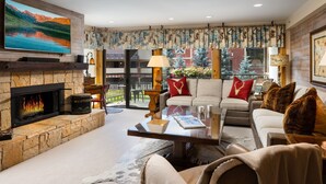 A cozy living room with a fireplace, comfortable seating, a flat-screen TV, and a balcony with a view of the mountains. - Montaneros 218 -2 Bedroom Diamond (Vail)