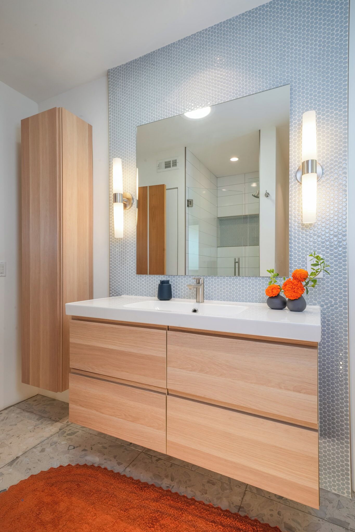 Une salle de bain moderne avec un grand miroir, un meuble-lavabo en bois et un pare-feu en carreaux.