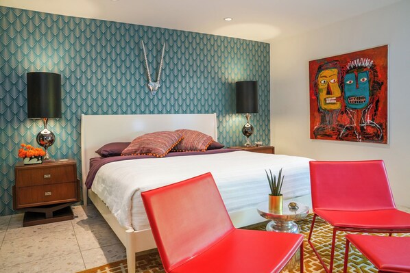 A modern hotel room with a large bed, two red chairs, a small table, and a painting on the wall. - Mid-Century Luxury Condo near Downtown Palm Springs (Palm Springs)