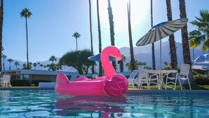Une piscine avec un flotteur en forme de flamant rose, des palmiers et un parasol de plage.