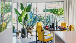 Un espace repas moderne avec une grande fenêtre, une table ronde, des chaises jaunes et une plante en pot.