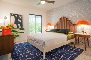 A bedroom with a bed, two bedside lamps, a ceiling fan, a window, and a decorative wall panel. - Mid-Century Luxury Condo near Downtown Palm Springs (Palm Springs)