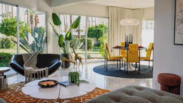 Un salon moderne avec un fauteuil en cuir noir, une table basse blanche et un coin repas avec des chaises jaunes.