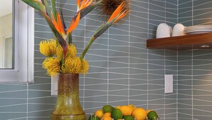 Une cuisine agrémentée d’un vase de fleurs, d’un saladier rempli d’oranges et d’un élément décoratif mural.