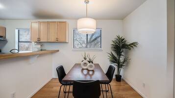 A dining area with a wooden table, black chairs, a pendant light, and a potted plant.
