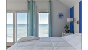 Una camera da letto con un letto, vista sul mare, una sveglia al muro e un piccolo tavolino con una pianta.