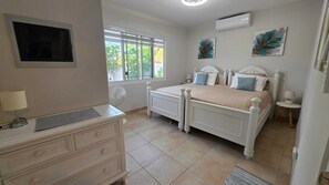 Une chambre à coucher comprenant un lit, des tables de chevet, une commode, une fenêtre et des œuvres d’art accrochées aux murs.