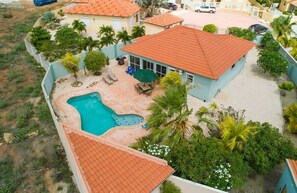 Une propriété résidentielle dotée d’une piscine, d’une terrasse avec mobilier d’extérieur et d’un toit recouvert de tuiles rouges.