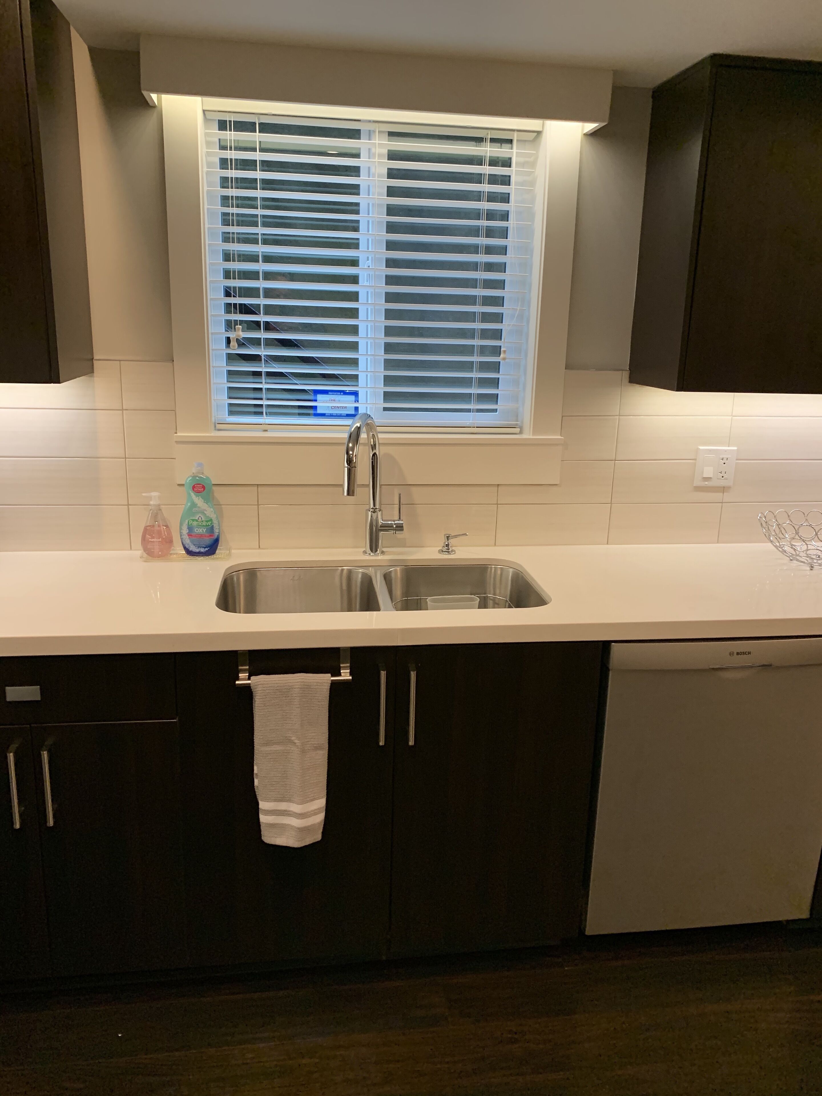 A kitchen with a stainless steel sink, a window with blinds, and a Bosch dishwasher.