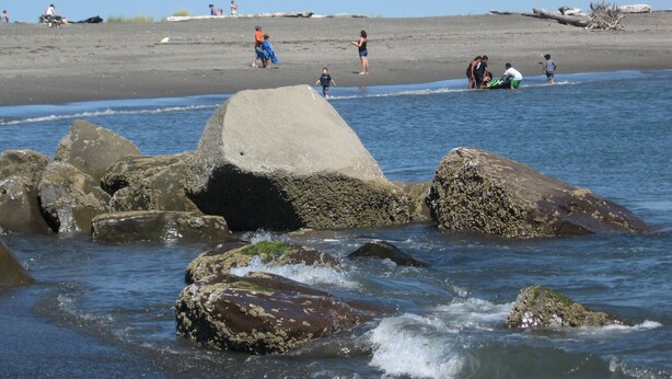 Una playa con rocas grandes al frente y gente de fondo.