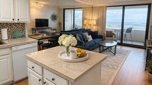A modern kitchen with a central island, white cabinetry, and a dining area with a blue sofa and a view of the ocean. - Wow!!! Updated Beach Front Resort 3rd Fl Condo with amazing view. (Destin)