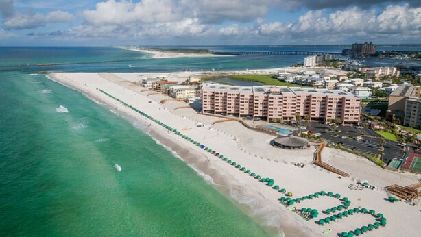An aerial view of a coastal resort with a long sandy beach, a marina, and a large hotel complex with multiple buildings. - Wow!!! Updated Beach Front Resort 3rd Fl Condo with amazing view. (Destin)