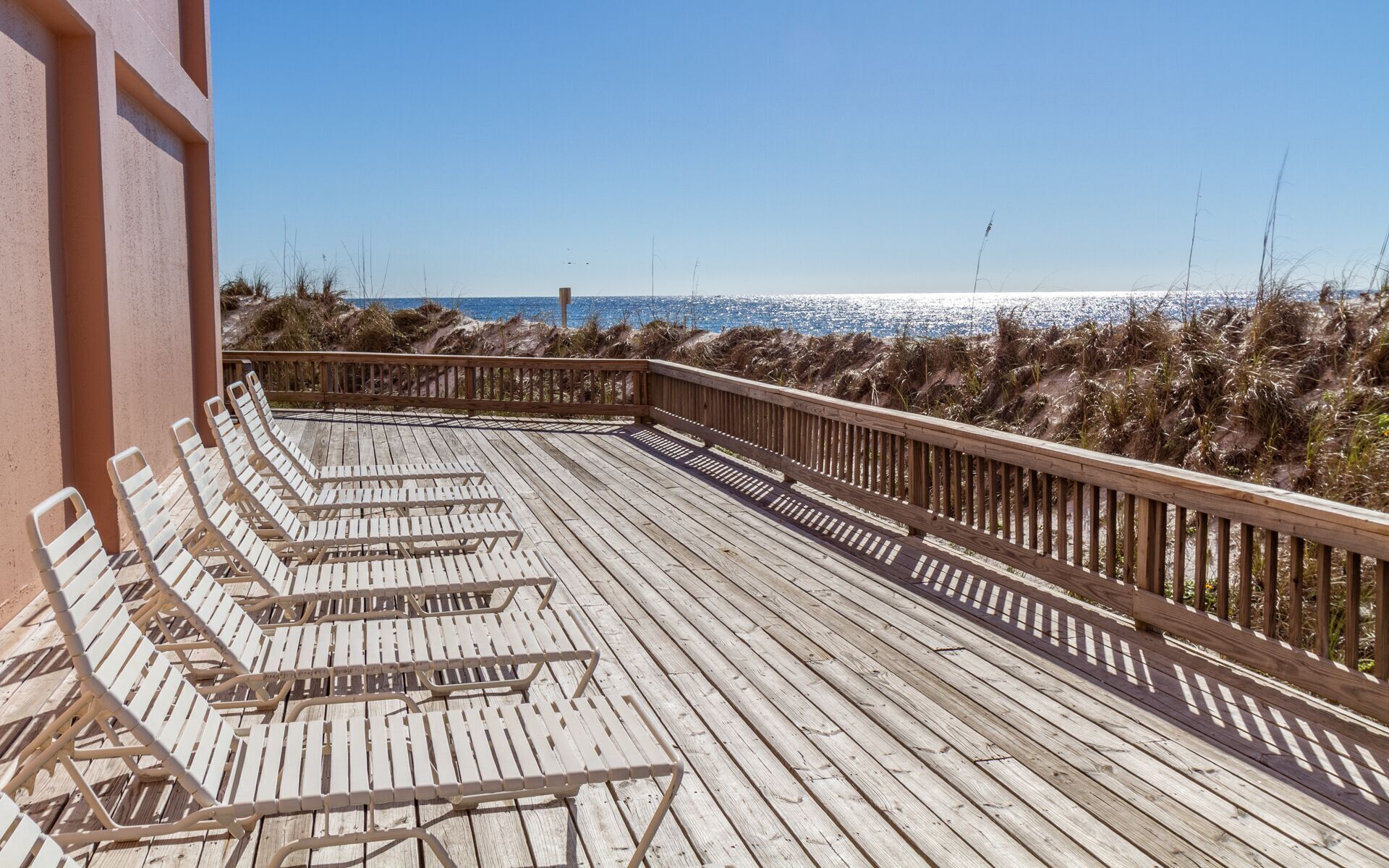 Una terraza de madera con sillones de descanso, barandilla de madera y vista a la playa y al océano.