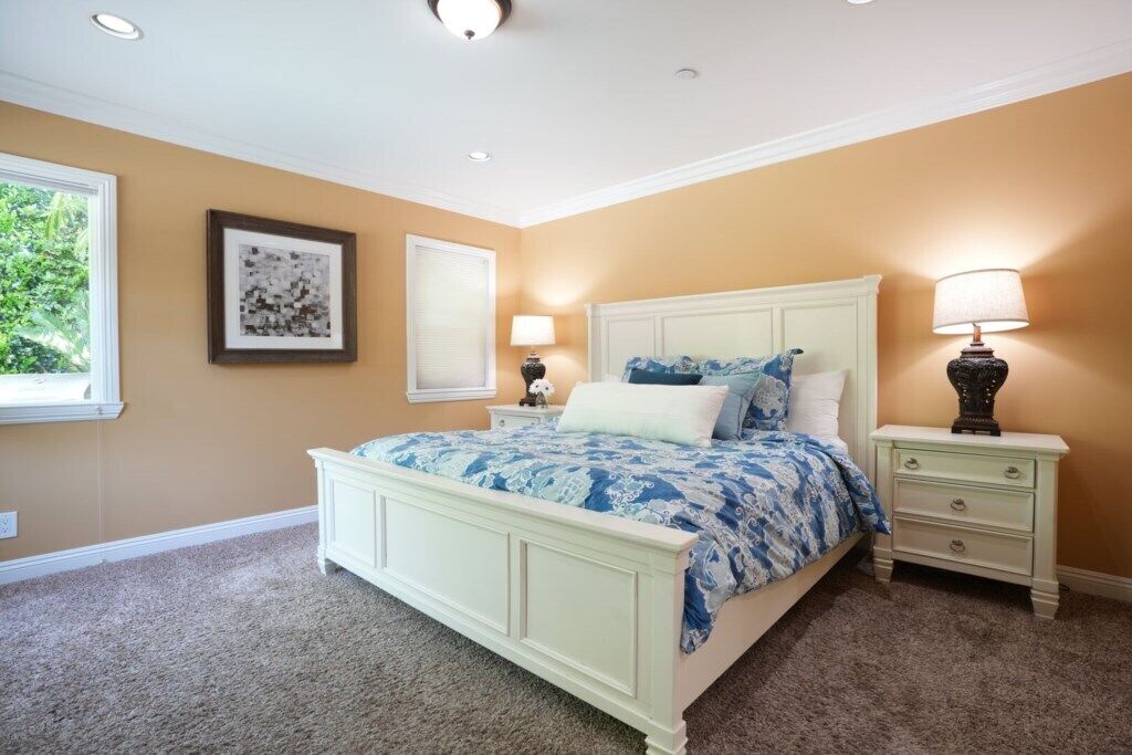 Une chambre à coucher avec un lit, des tables de chevet, une fenêtre et un tableau encadré au mur.