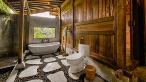 A rustic bathroom with a stone-tiled floor, a freestanding bathtub, and a toilet. - Mandana Ubud Villa (Ubud)