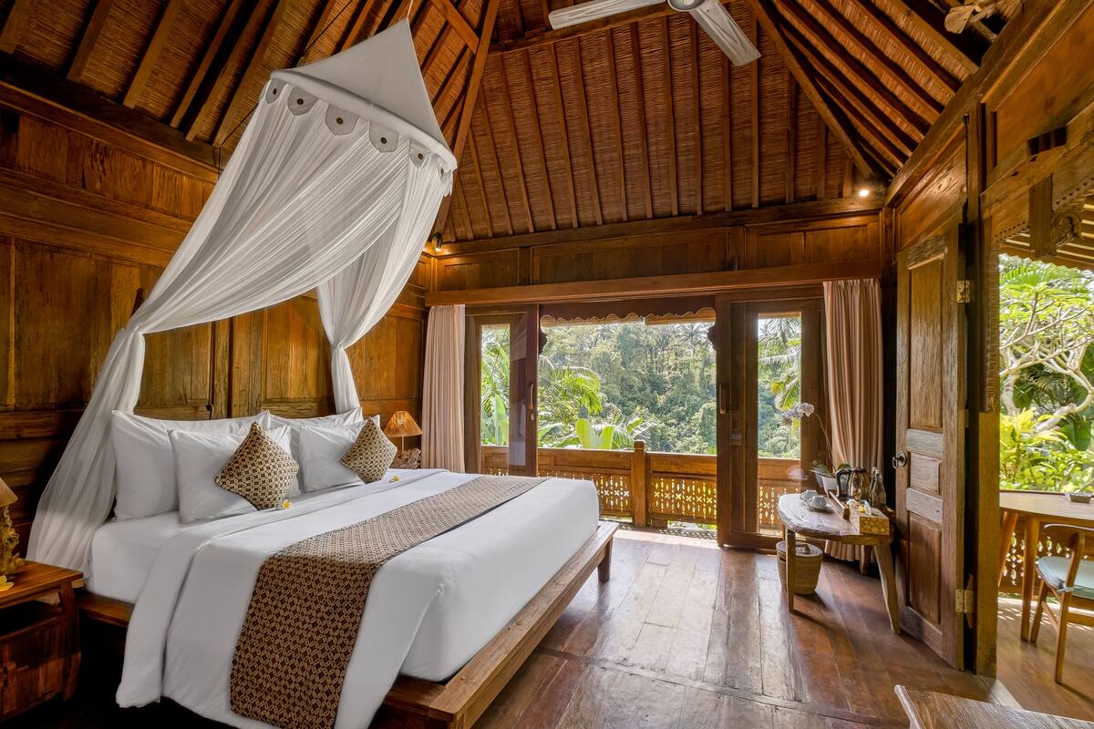 A wooden bedroom with a canopy bed, large windows, and a view of the outdoors.