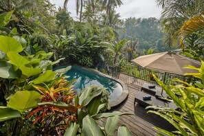 A pool surrounded by lush tropical plants, wooden deck, and lounge chairs. - Mandana Ubud Villa (Ubud)