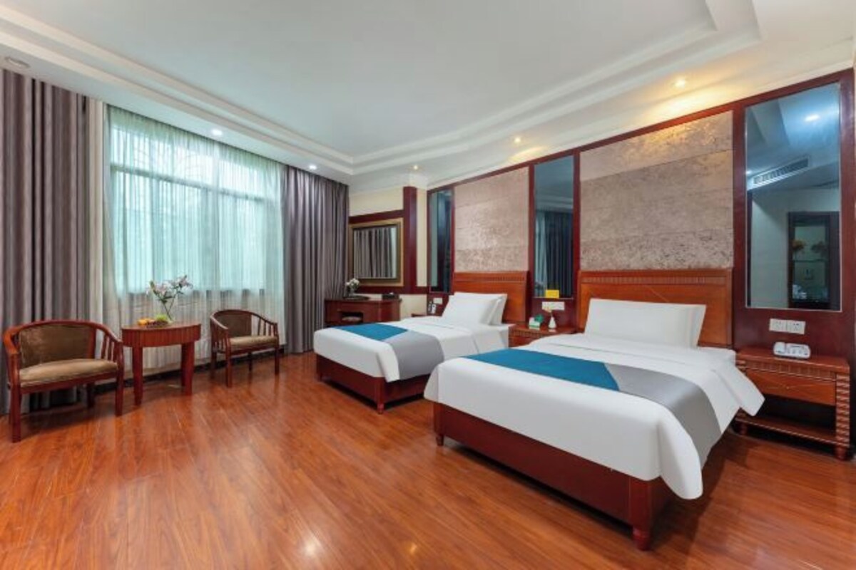 Habitación de hotel con dos camas, suelo de madera, escritorio, sillas y un espejo grande.