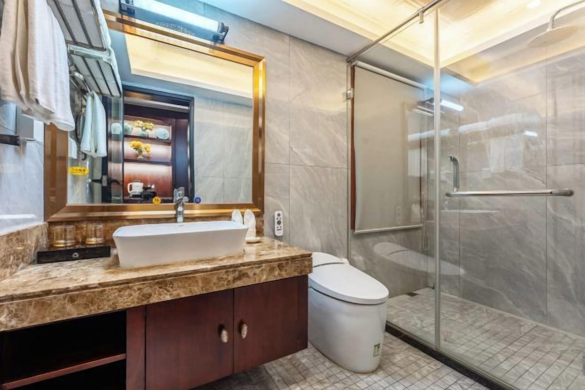 Un baño moderno con un lavabo de mármol, un espejo grande, un inodoro y una ducha con mampara de cristal.