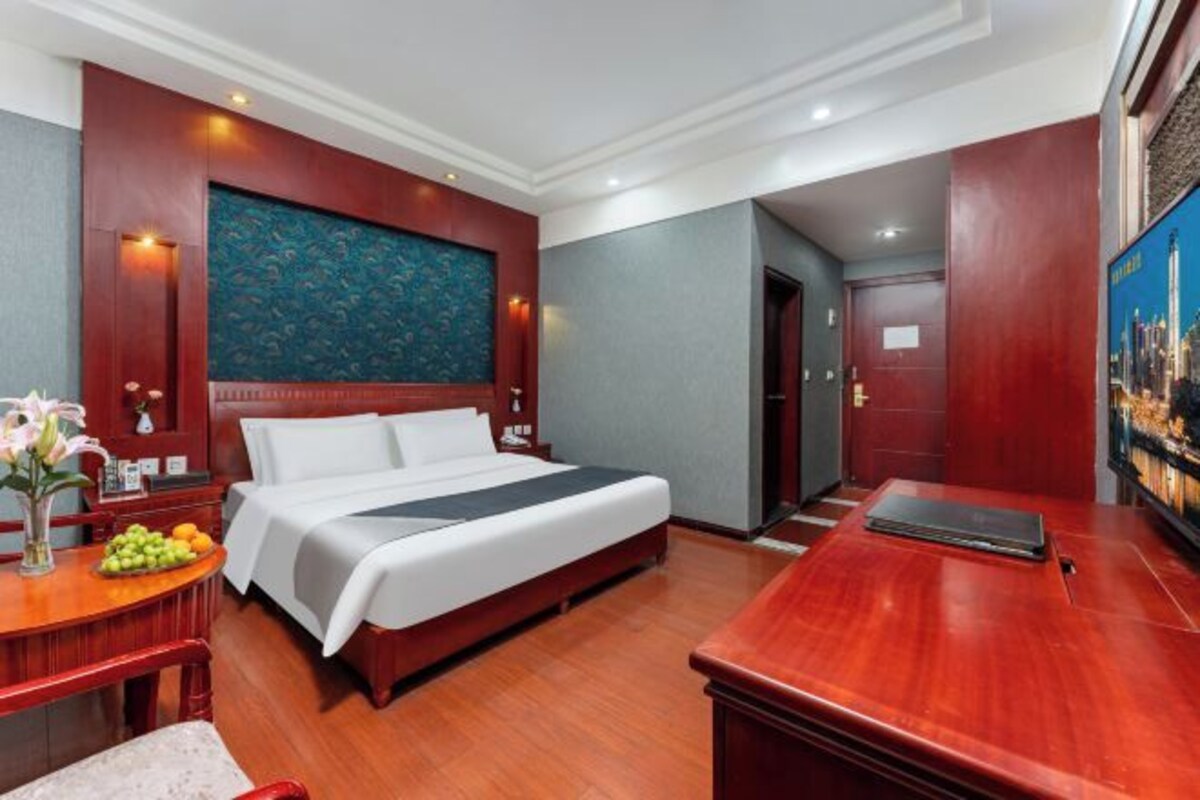 Habitación de hotel con una cama grande, un escritorio con una computadora portátil, un frutero y un cuadro en la pared.