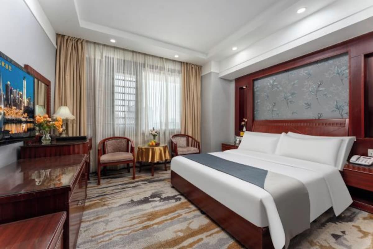 Habitación de hotel con una cama grande, un escritorio, dos sillas, una mesita con flores y un cuadro en la pared.